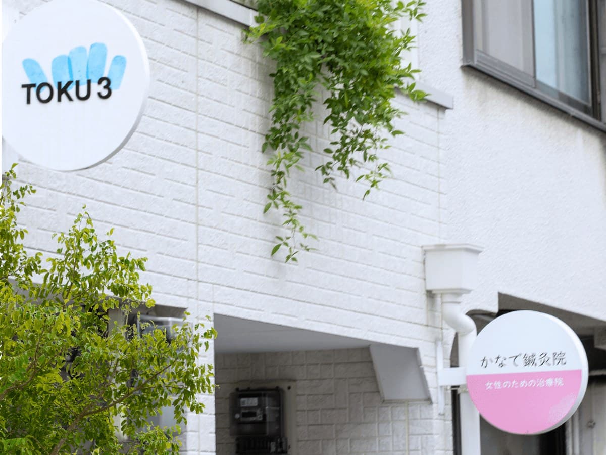 白い館の外観。白い壁に掛かるサロンの看板と、窓辺の緑
